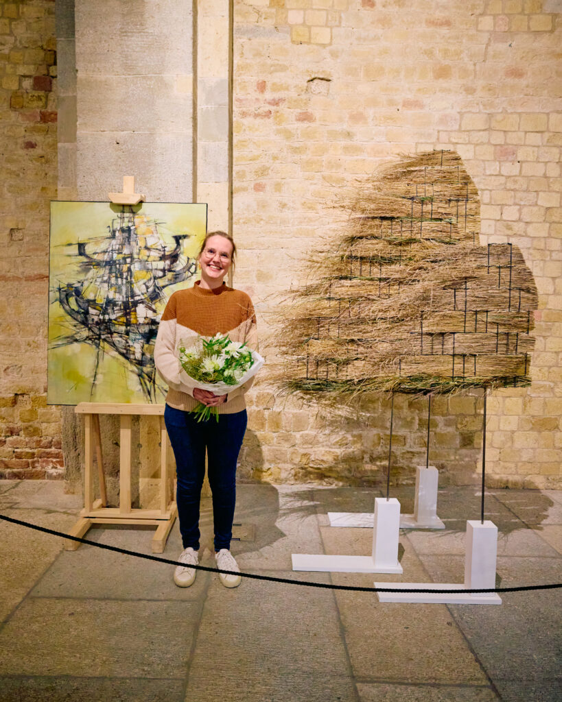 Anita Schött devant sa création florale primée et le tableau Les jonques de Simone Degal lors de De Vert et d’Art 2024