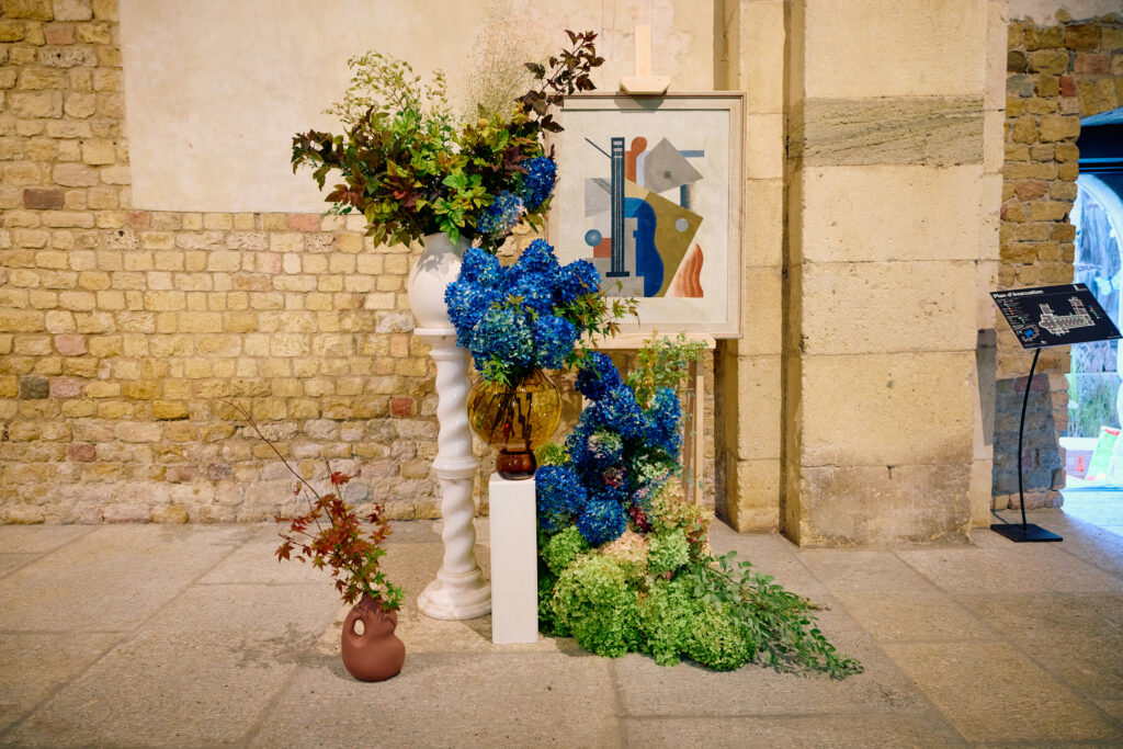 Composition florale aux hortensias bleus présentée à côté d’un tableau dans l’Abbatiale de Payerne lors de De Vert et d’Art 2024